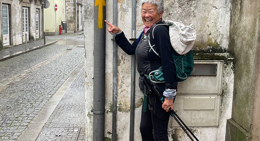 pilgrim pointing to arrow marker that shows the Camino route